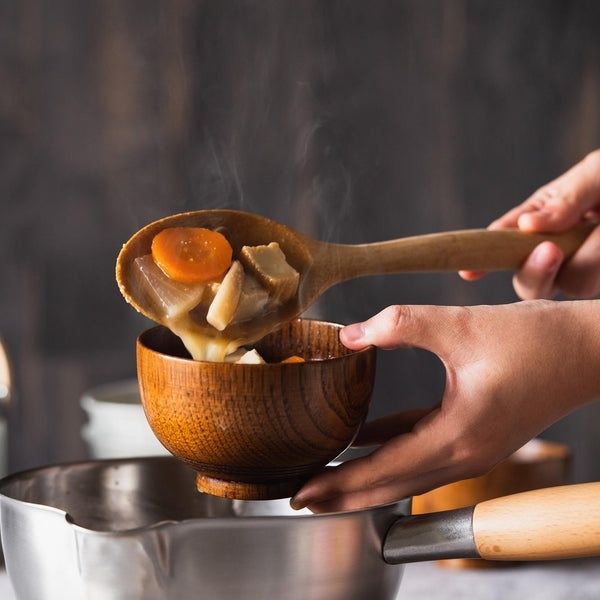 Holzlöffel mit heißer Brühe, Gemüse und Pilzen über einer Schüssel