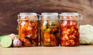Drei Gläser mit selbst gemachtem Kimchi neben Limette, Knoblauch und Kohl
