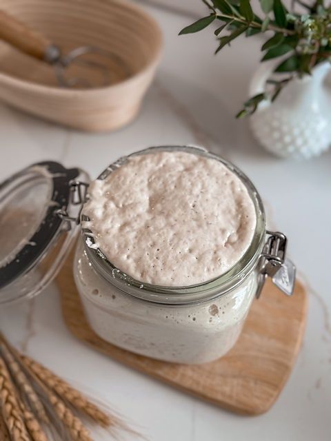Blubbernder Sauerteigstarter in einem offenen Bügelglas auf einem Holzbrett